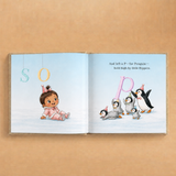 An open children's book spread on a warm tan background. The left page shows a baby sitting on snow with hanging letters 'S' and 'O', and the right page shows penguins with the text, 'And left a P—for Penguin—held high by little flippers.